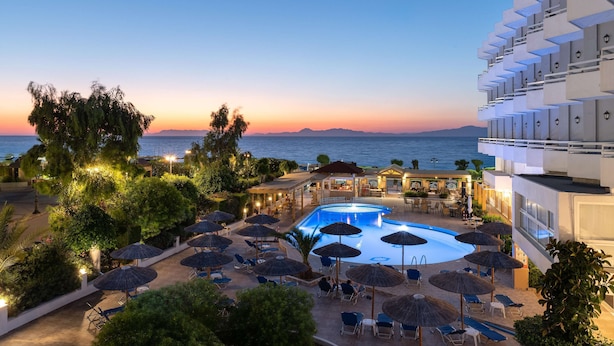 A resort pool area with a view of the sea at sunset, surrounded by lounge chairs and umbrellas. - Lito Hotel (Rhodes)