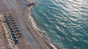 An aerial view of a beach with rows of umbrellas and lounge chairs along the shoreline. - Lito Hotel (Rhodes)