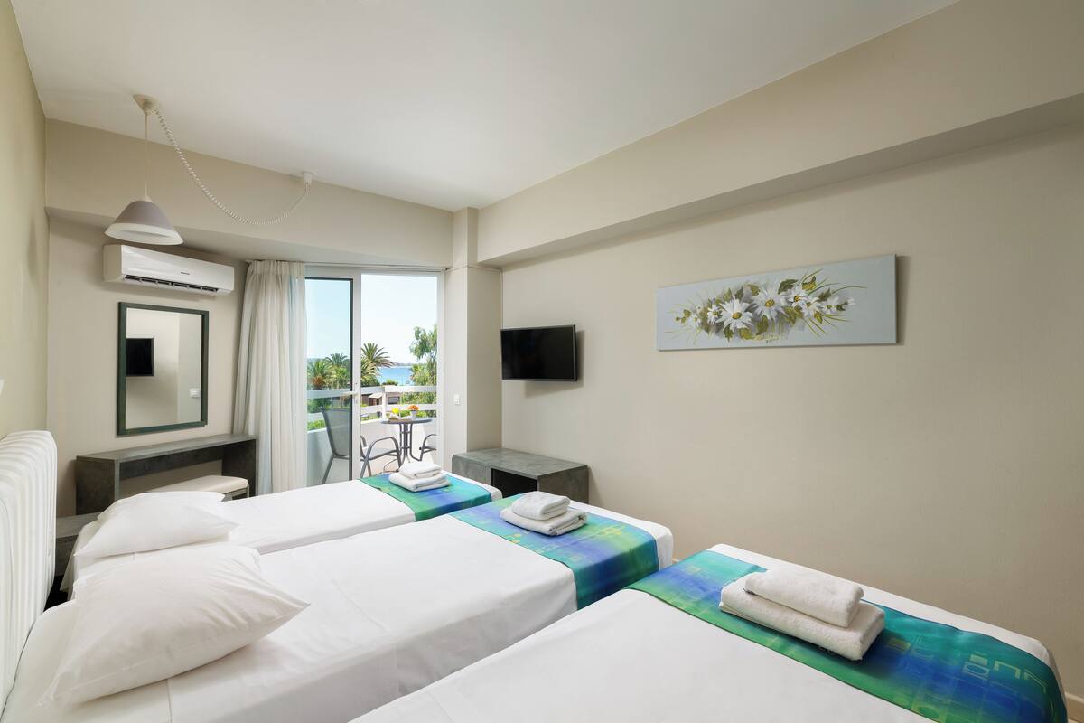 Habitación de hotel con dos camas, un escritorio, una silla, un televisor y un balcón con vistas.