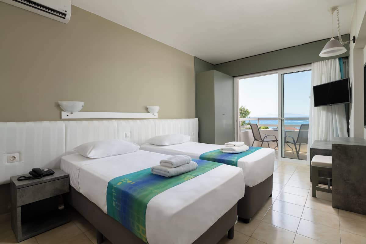 Habitación de hotel con dos camas, un escritorio, una silla, un televisor y un balcón con vistas.