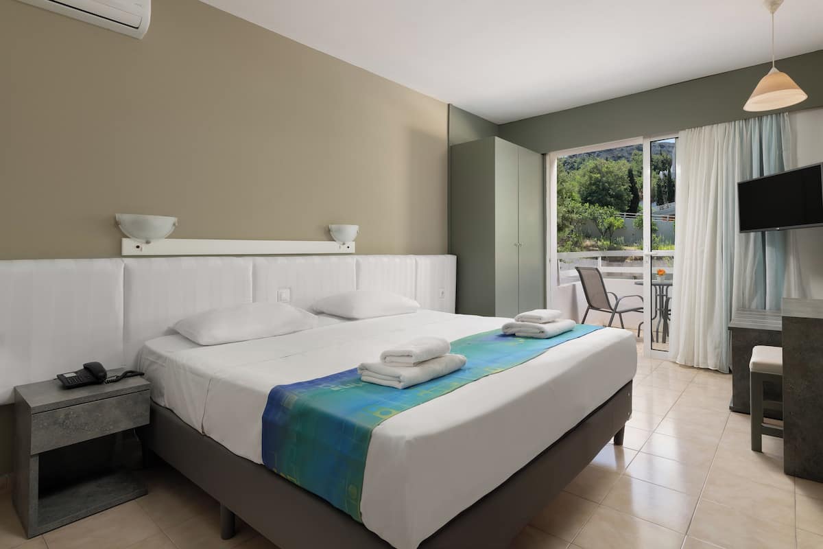Habitación de hotel con una cama, una mesita de noche con teléfono, televisión y vistas al exterior.