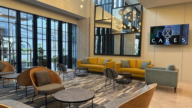 A modern lobby with large windows, a yellow sofa, and a TV displaying 'ASCOTT CARES'. - Citadines Connect Airport Jakarta (Jakarta)