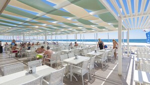 An outdoor dining area with white tables and chairs, a striped ceiling, and a view of the beach and ocean. - Terrace Elite Resort - All Inclusive (Manavgat)