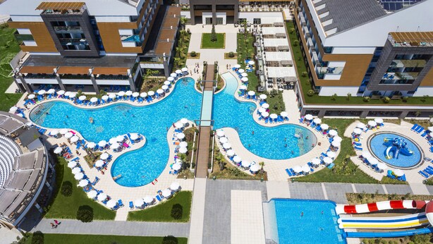 A large swimming pool with a slide, surrounded by lounge chairs and umbrellas, and a connecting walkway. - Terrace Elite Resort - All Inclusive (Manavgat)
