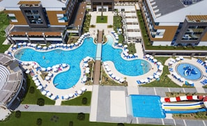Une grande piscine avec un toboggan, entourée de chaises longues et de parasols, et reliée à une passerelle.