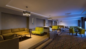 Un hall d’hôtel moderne, doté d’un canapé, de fauteuils, d’une table basse et d’un espace repas avec des tables et des chaises.