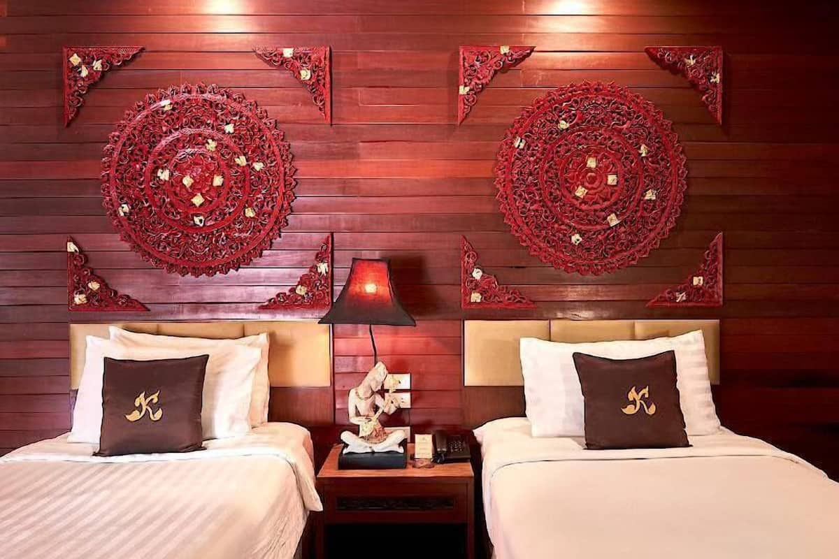 A hotel room with two beds, a nightstand with a lamp, and decorative wall panels.