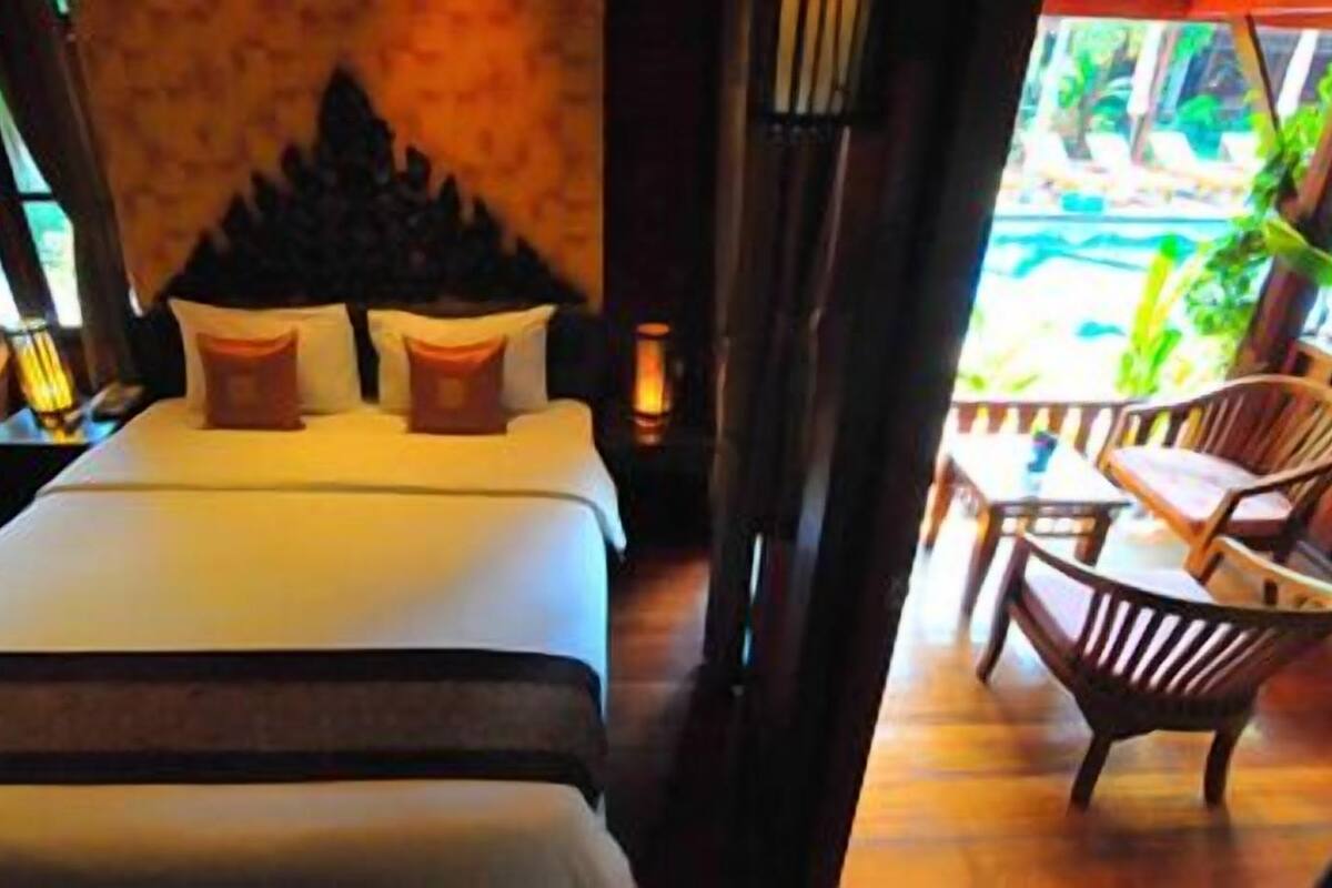 A bedroom with a bed, pillows, a nightstand, and a view of a pool and outdoor seating area.