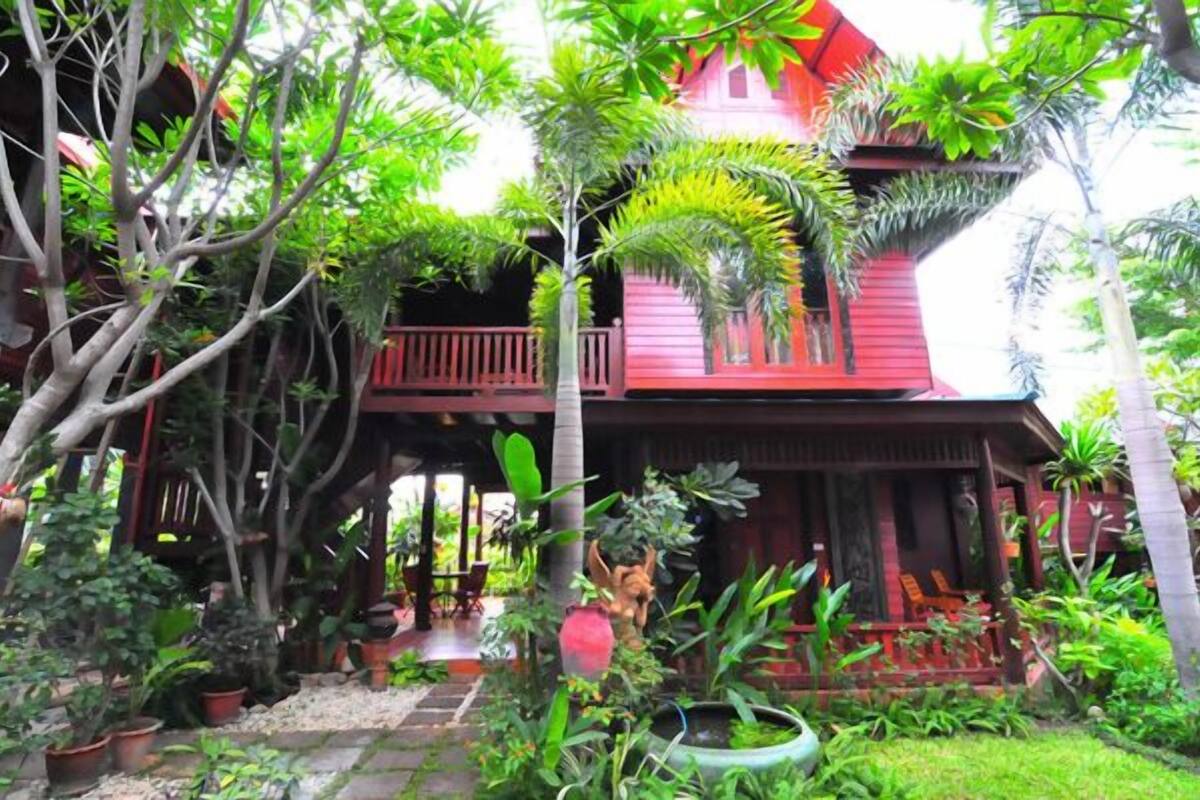 A red wooden house surrounded by lush greenery and plants.