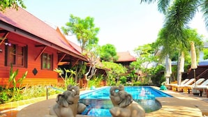 A pool area with two elephant statues, a red building, and palm trees. - Ruen Kanok Thai House (Hua Hin)