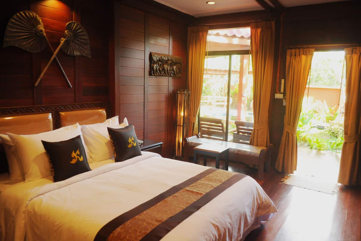 A hotel room with a large bed, a wooden headboard, a small table, and a view of the outdoors through a sliding door.