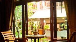 A room with wooden flooring, two wooden chairs, a small round table, and a window with curtains. - Ruen Kanok Thai House (Hua Hin)