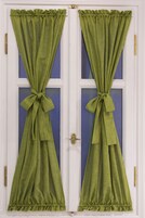 Una puerta con cortinas verdes atadas en lazos, un picaporte de bronce y un panel de ventana azul.