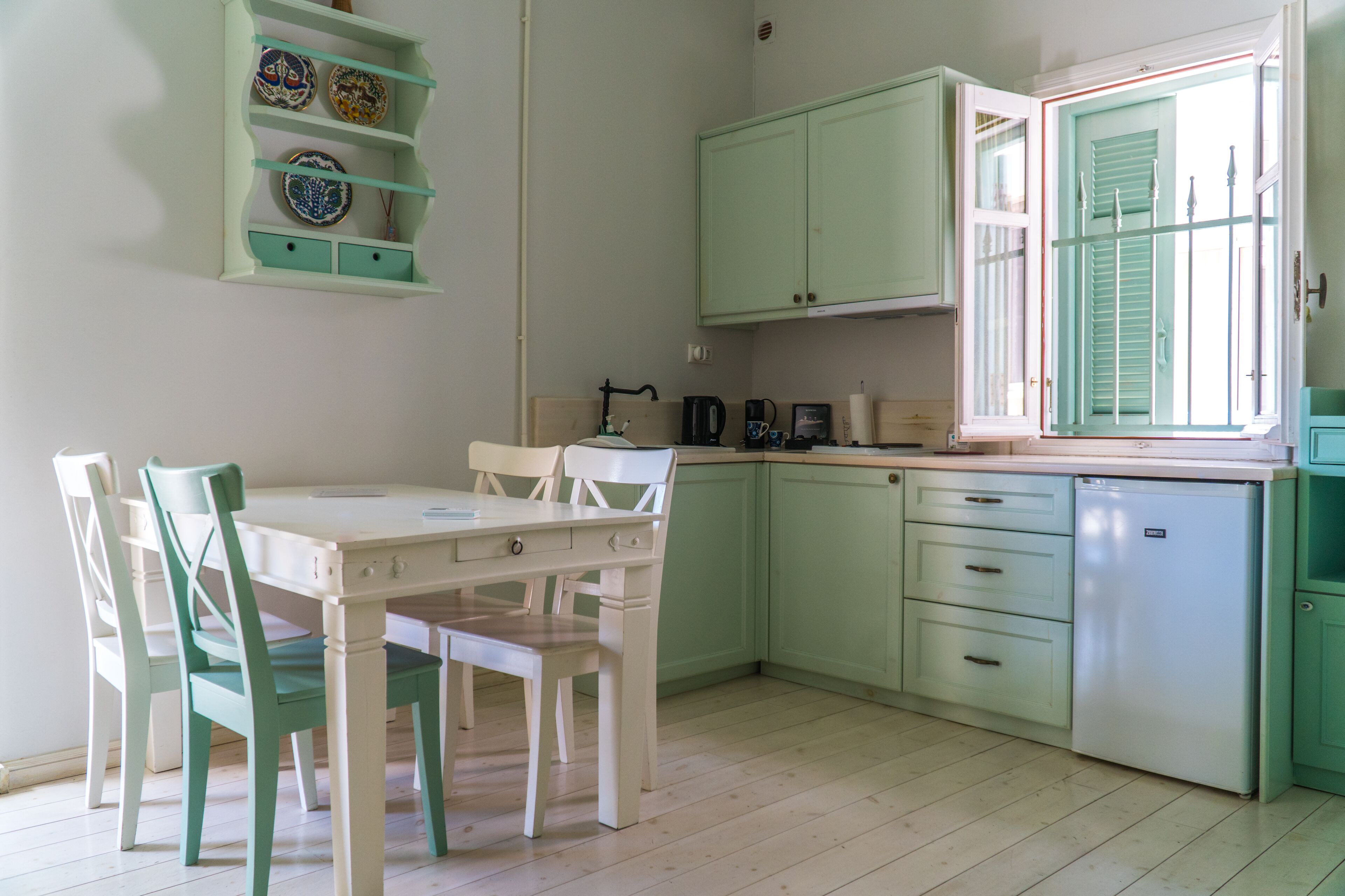 Una cocina con una mesa de comedor y sillas, una cafetera y un refrigerador.
