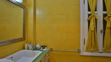 A bathroom with yellow tiles, a white sink, a mirror, and yellow curtains tied at the window.