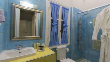 Un baño con un lavamanos amarillo, un inodoro blanco, cortinas de ducha azules y un albornoz blanco colgado en la pared.