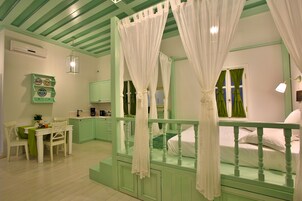 Un dormitorio con cama con dosel, una pequeña zona de estar con mesa y sillas, y una kitchenette al fondo.