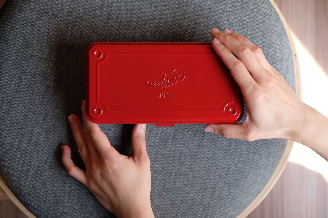 Ein roter Koffer mit der Aufschrift "Paddle Hotel", platziert auf einem runden Holzhocker.
