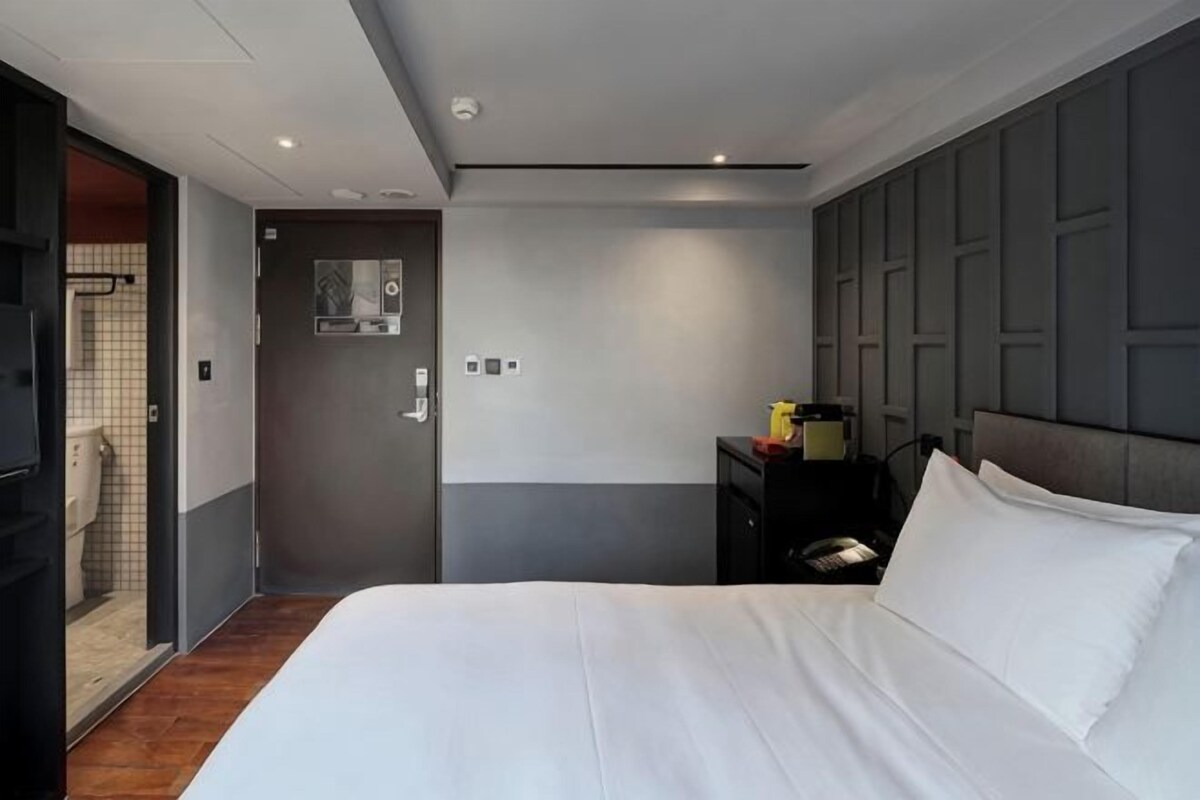A hotel room with a bed, a nightstand, a mirror, and a door leading to a bathroom.
