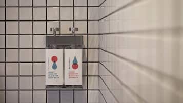 En flisebeklædt væg med to dispensere mærket 'Honey Murcott Black Tea Body Wash' og 'Honey Murcott Black Tea Shampoo'.