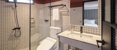 Ein modernes Badezimmer mit Duschkabine aus Glas, einer weißen Toilette, einem Waschbecken inklusive Spiegel und einem Handtuchhalter.