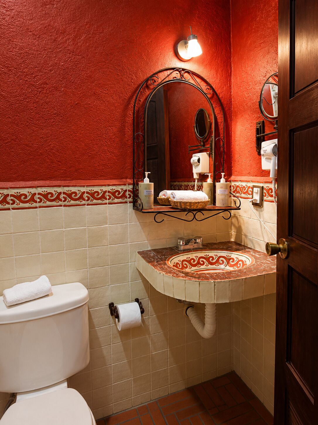 A bathroom with a red wall, a white toilet, a sink with a decorative tile backsplash, and a mirror.