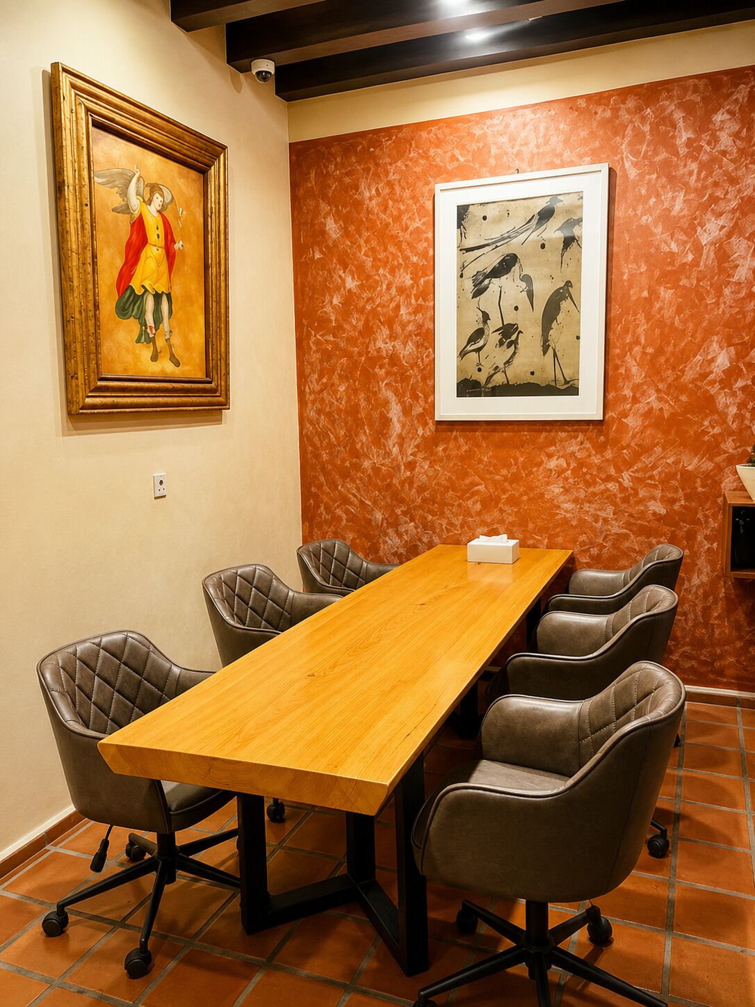 A conference room with a long wooden table, six leather chairs, and two framed artworks on the walls.