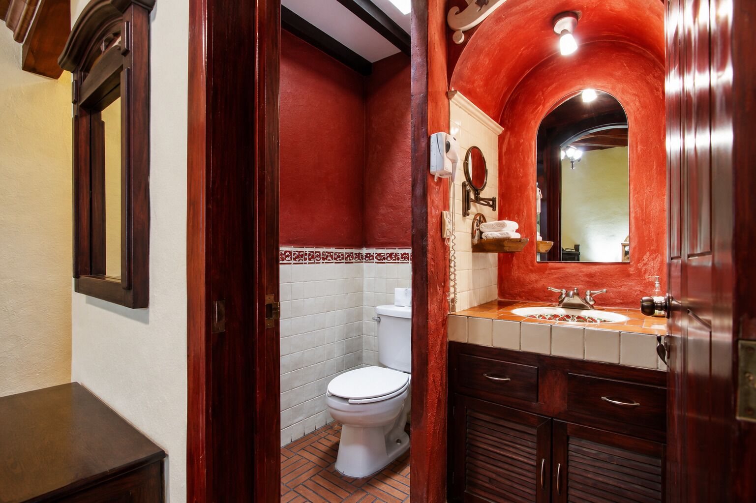 Un bagno con il water bianco, un mobile bagno in legno con specchio e una parete decorata in rosso.