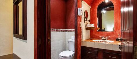 Un bagno con il water bianco, un mobile bagno in legno con specchio e una parete decorata in rosso.