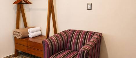 A room with a striped armchair, a wooden bench with towels, and a wall-mounted wooden rack.