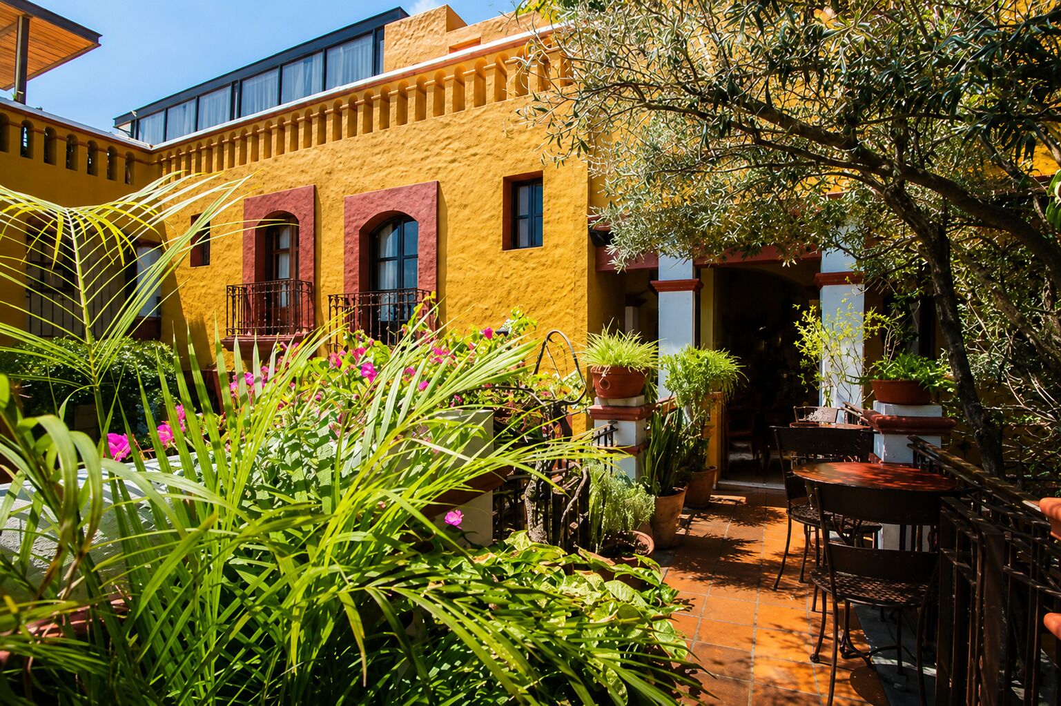 Une cour avec un bâtiment jaune, des plantes en pot et du mobilier d’extérieur.
