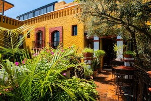 A courtyard with a yellow building, potted plants, and outdoor furniture. - Hotel Casa del Sótano (Oaxaca)