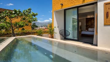 Una piscina moderna con agua cristalina, rodeada por un edificio de fachada amarilla y grandes puertas de vidrio que dan a un dormitorio.