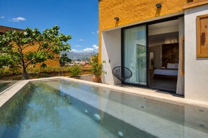 A modern pool with clear water, surrounded by a building with a yellow exterior and large glass doors leading to a bedroom.