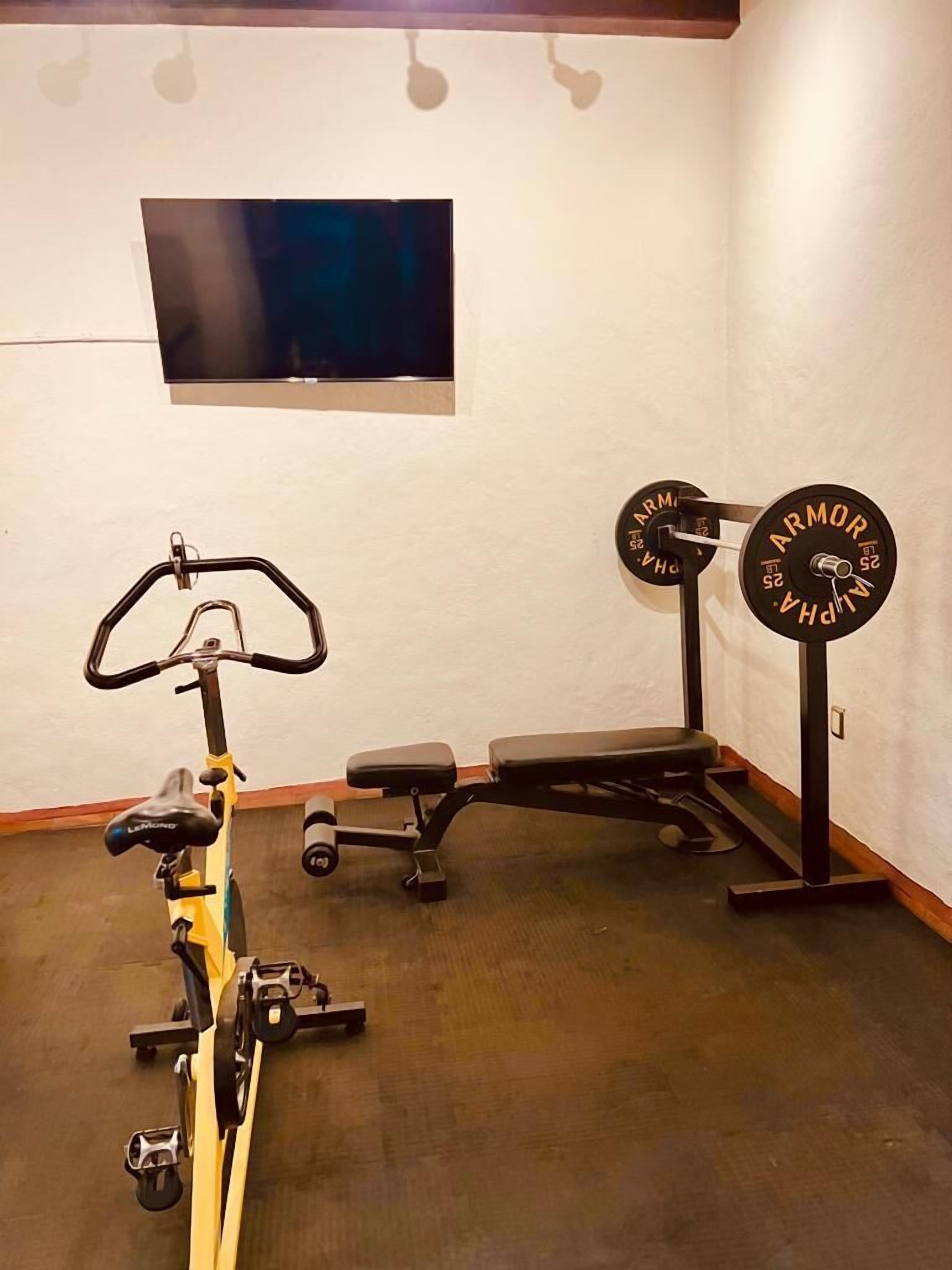 Un gimnasio en casa con una bicicleta estática, una banca y una camilla de pesas con barra.