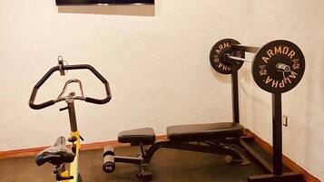 Un gimnasio en casa con una bicicleta estática, una banca y una camilla de pesas con barra.