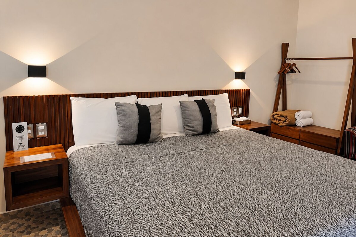 A hotel room with a large bed, two bedside tables, a wooden headboard, and a wall-mounted lamp.