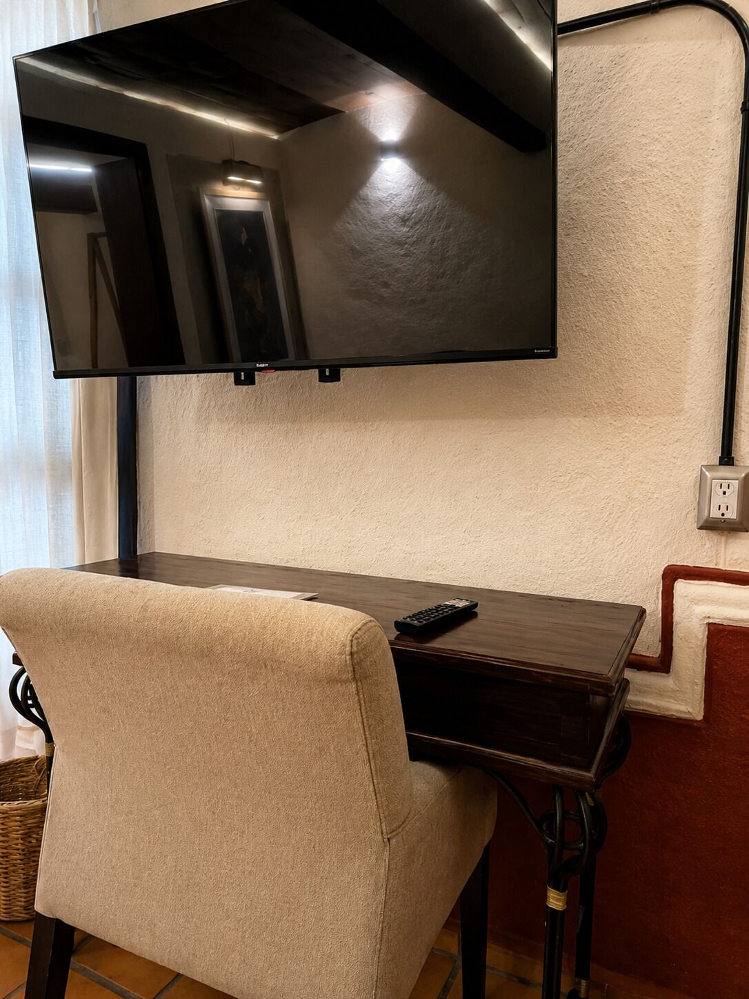A flat-screen TV mounted on a wall above a wooden table with a remote control on it.