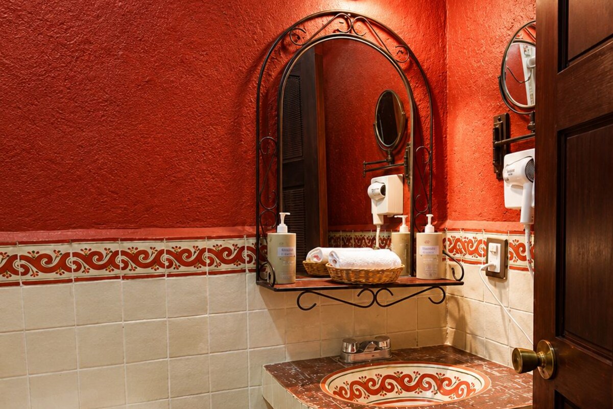 A bathroom with a red wall, a white toilet, a sink with a decorative tile backsplash, and a mirror.
