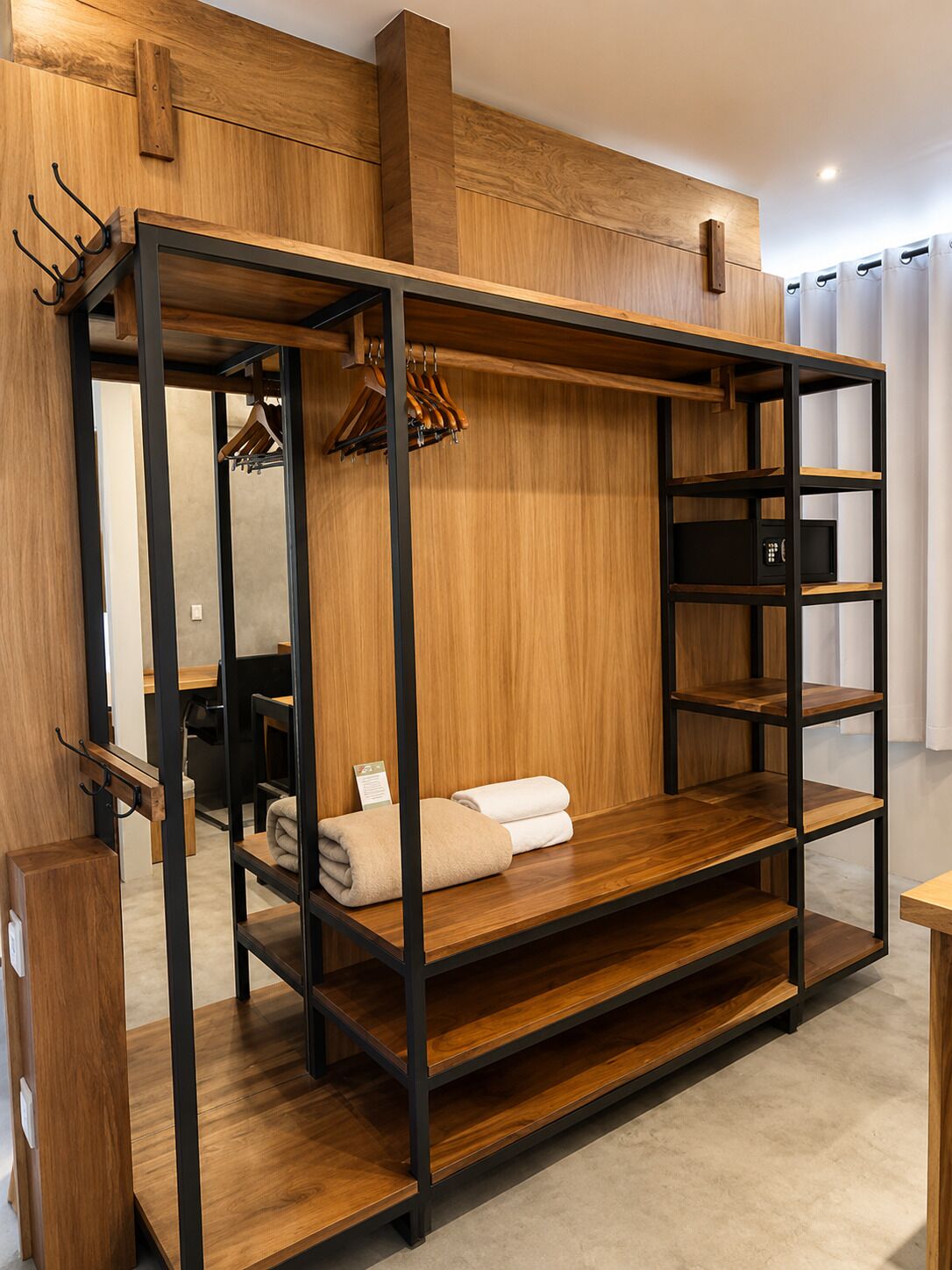 Una cama litera con estructura de madera y estantes, un escritorio pequeño y un perchero.