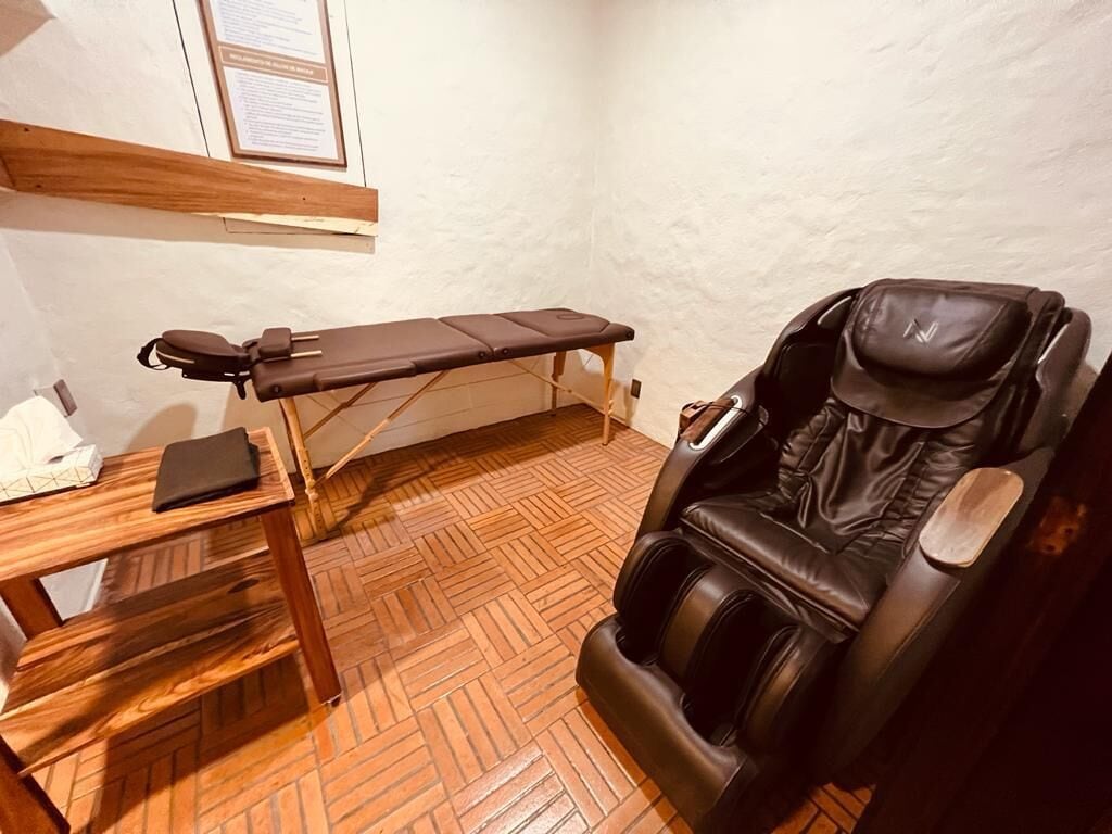 Un cuarto de terapia de masajes con suelo de madera, una camilla y una silla de masaje.