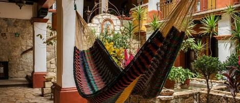 A hammock hanging between columns in a courtyard with stone flooring and potted plants.