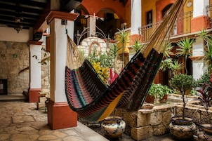 A hammock hanging between columns in a courtyard with stone flooring and potted plants.