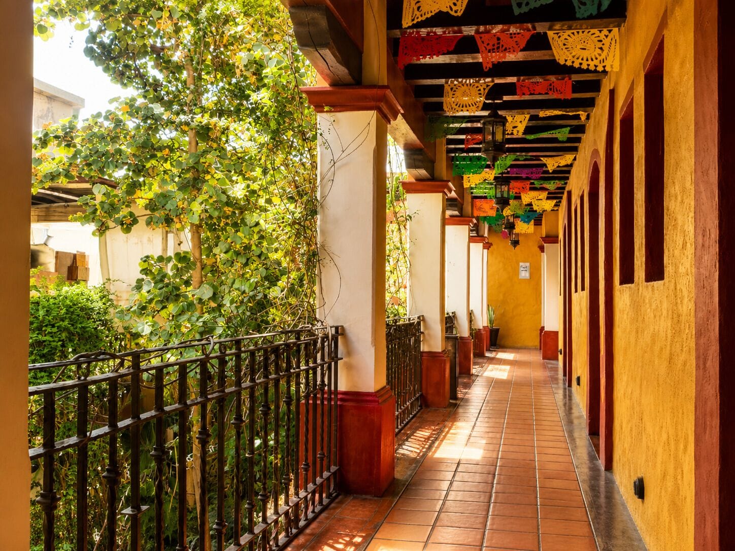 A corridor with tiled flooring, a metal railing, and a row of arches.
