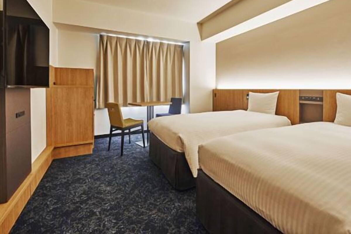 A hotel room with two beds, a desk, a chair, a TV, and a wardrobe.