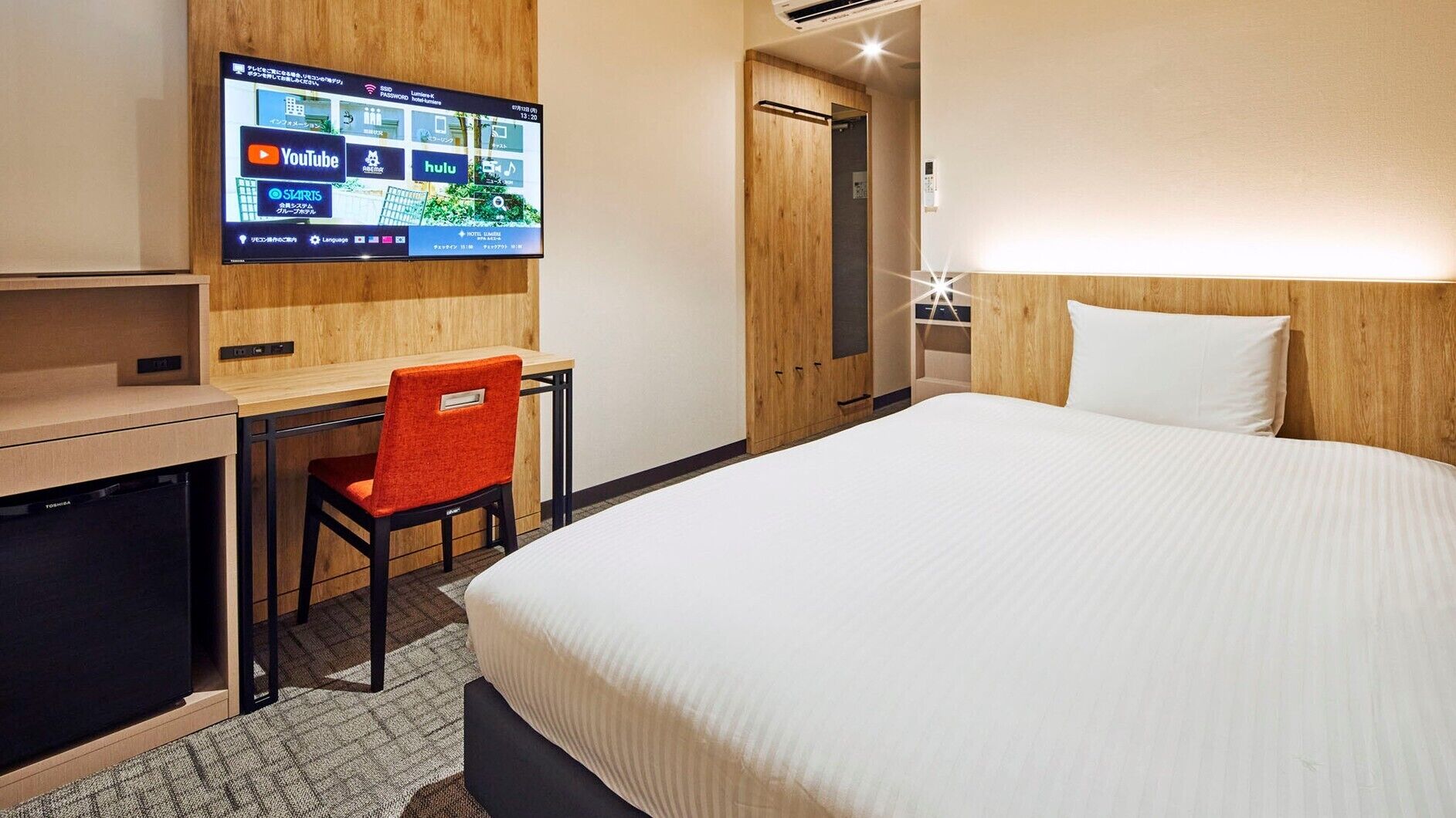 Une chambre d’hôtel comprenant un lit, un bureau avec une chaise, un téléviseur permettant d’accéder à des services de diffusion en continu et une armoire en bois.