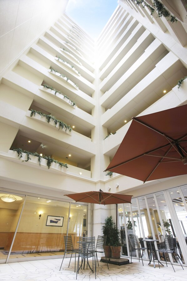 Un atrium à plusieurs niveaux, doté de murs en verre, d’un espace extérieur aménagé et de plantes en pot.