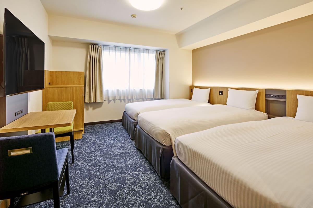 A hotel room with two beds, a desk, a chair, a television, and a window with curtains.