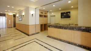 A hotel lobby with a reception desk, a television mounted on the wall, and a tiled floor. - Hotel Lumiere Kasai (Tokyo)