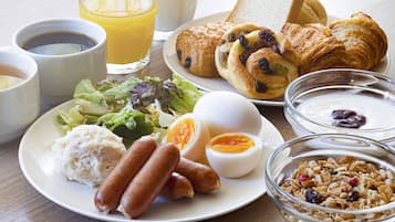 A breakfast plate with croissants, eggs, sausages, and a bowl of cereal.